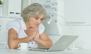 Starsza pani z zaciekawieniem patrzy na laptopa, szukając informacji, ile trwa staż z urzędu pracy.