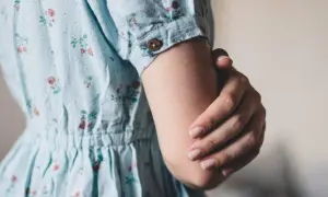 Een vrouw in een bloemenjurk houdt haar arm vast, misschien om oefeningen tegen trillende handen te doen.