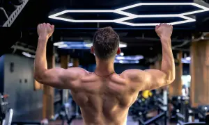 Mężczyzna wykonuje ćwiczenie scapular pull ups na drążku, budując silne plecy i ramiona w nowoczesnej siłowni.