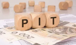Drewniane klocki z literami "PIT" leżą na banknotach 200 zł i dokumentach podatkowych. To symboliczne przedstawienie rozliczenia podatku, gdzie darowizna może wpłynąć na Twój PIT.