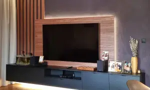 Nowoczesny salon z telewizorem w zabudowie meblowej. Drewniane panele i subtelne podświetlenie tworzą przytulną atmosferę.