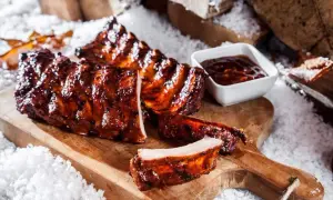 Saftige spareribs im backofen, glasiert und mit BBQ-Sauce, auf einem Holzbrett mit Schnee dekoriert.
