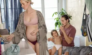 Gravid kvinna vid handfatet, en man borstar sitt barns tänder. En familj förbereder sig för dagen.