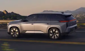 Srebrny Toyota Highlander jedzie po drodze z górzystym krajobrazem w tle. Sprawdź aktualną toyota highlander cena!