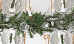 Sencillo decoracion mesa navidad con ramas de pino, piñas y velas. Vajilla gris, servilletas blancas con detalle de romero y cubertería dorada.