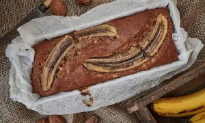 Nybakad banankaka i form, toppad med bananskivor. Valnötter och en gammal kniv ligger bredvid. Perfekt att baka med banan!