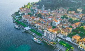 Urokliwe como miasto nad jeziorem, z kolorowymi budynkami, zielenią i łodziami przy nabrzeżu.