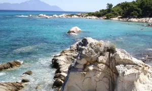 Słoneczne Chalkidiki plaże z turkusową wodą, skałami i ludźmi kąpiącymi się w morzu. W oddali widać góry.