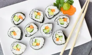 Zestaw do robienia sushi w domu: świeże rolki z awokado, ogórkiem i marchewką, podane z wasabi i pałeczkami.
