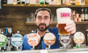 Barista con una birra in mano, pronto a versare nei bicchieri. Dietro di lui, una selezione di birre artigianali.