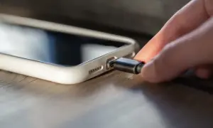 Une main insère un câble dans la connectique d'un iPhone 13, prêt à le recharger.