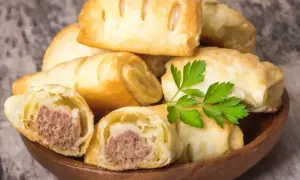 Stos pieczonego ciasta francuskiego z kiełbasą w środku, ozdobione natką pietruszki. Idealne na szybką przekąskę.