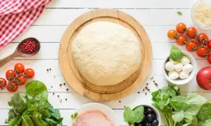 Surowe ciasto na pizzę z pomidorkami, mozzarellą, oliwkami i bazylią na białym tle.