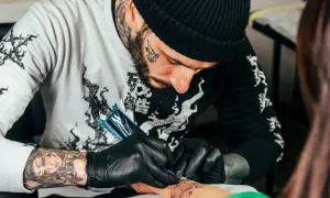 Artysta z tatuażami na twarzy i rękach tworzy nowy wzór na przedramieniu klienta. Dyskutują o cukrzycy a tatuażu.