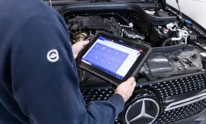 Tecnico esegue la revisione auto con tablet diagnostico, controllando i sistemi del motore.