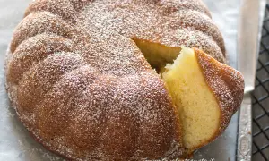 Una soffice torta allo yogurt, cosparsa di zucchero a velo, con una fetta tagliata che ne rivela l'interno dorato e profumato.