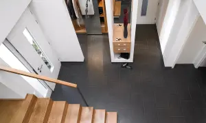Moderner Flur nach Renovierung: Holzboden, dunkle Fliesen, Garderobe mit Spiegel und Blumen.