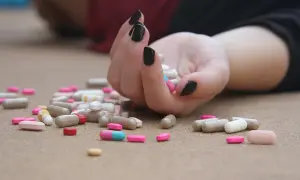 Dłoń z czarnymi paznokciami, rozsypane tabletki, w tym kapsułki z sulpirydem, sugerują kryzys zdrowia psychicznego.