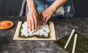 Ręce rozprowadzają ryż na nori, przygotowując się do zwinięcia sushi. Kluczowe jest, ile gotować ryż do sushi, by był idealny.