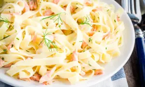 Tagliatelle mit Lachs, garniert mit Dill und Schnittlauch, auf einem weißen Teller. Ein köstliches Gericht, das zum Genießen einlädt.