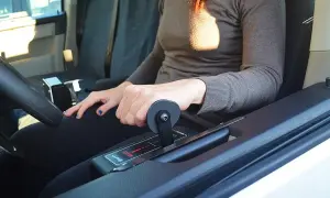 Mano che aziona la leva di un allestimento auto per disabili, con indicazioni "brake" e frecce.