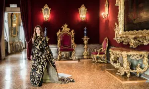 Donna con abito prezioso in una sala dorata, un'elegante tessitura Bevilacqua per una visita regale.