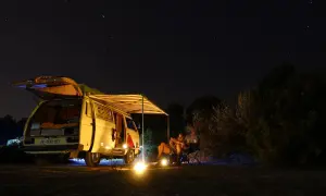 Sternenhimmel über einem Campervan mit ausgefahrener Markise. Ein Paar sitzt davor, die perfekte Mallorca Route für Camper.