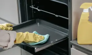 Rękawiczki i ściereczka pomagają w tym, jak wyczyścić blachę z piekarnika. Obok stoi żółta butelka ze sprayem.