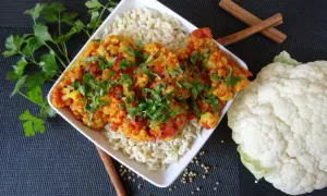 Aksamitne curry z kalafiora podane z ryżem, udekorowane świeżą natką pietruszki i czarnuszką. Obok leży świeży kalafior i laski cynamonu.
