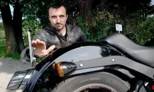 Mężczyzna w skórzanej kurtce pokazuje mocowanie tablicy motocyklowej.