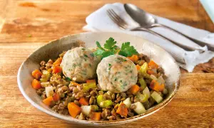 Zwei Semmelknödel auf Linsengemüse mit Karotten und Sellerie, garniert mit Petersilie.