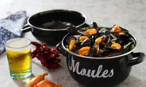 Un bicchiere di birra dorata accanto a cozze fumanti in una pentola nera, con peperoncini secchi e scalogni. Un perfetto abbinamento di birra e pesce.
