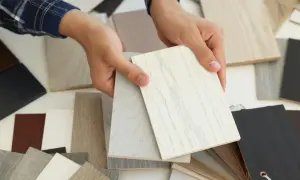Ręce trzymają próbki płyt meblowych, porównując ich faktury i kolory. Widać różne odcienie drewna i kamienia, co ułatwia wybór idealnych wymiarów do projektu.