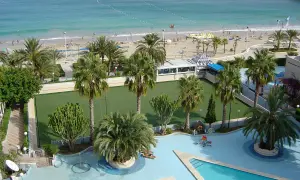 Vista aérea de un resort con piscina, cancha de césped, palmeras y una playa con el mar azul. Un lugar perfecto para sol y mar spa.