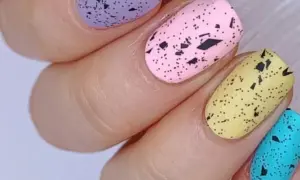 Delikatne, **milky nails** w pastelowych kolorach: fioletowym, różowym, żółtym i turkusowym, ozdobione czarnymi plamkami imitującymi skorupki jajek.