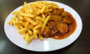 Eine Portion knuspriger Pommes Frites neben einer Currywurst in würziger Sauce, ein Klassiker aus Berlin.