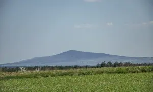 Łagodne, zalesione góry świętokrzyskie szczyty na horyzoncie, z zieloną łąką na pierwszym planie.