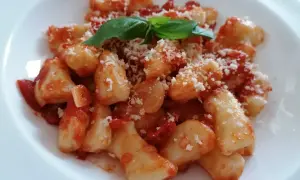 Pyszne gnocchi w sosie pomidorowym, posypane parmezanem i udekorowane listkiem bazylii.