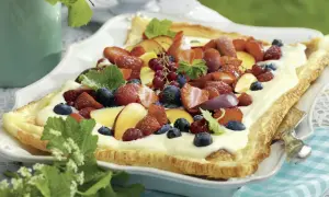 En långpanna med tårtbotten täckt av kräm och färska bär som jordgubbar, blåbär och hallon.