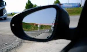 Blick in den Rückspiegel: Ein LKW fährt vorbei. Die rote Linie zeigt, wie man das Spiegelglas richtig einstellen kann, um die Straße im Blick zu behalten.