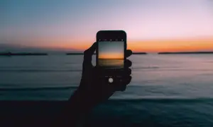 Dłoń trzyma smartfon, na którym widać zdjęcie wschodu słońca nad morzem.