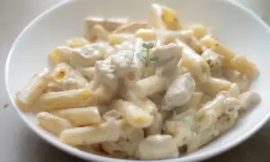 Penne z kurczakiem w kremowym sosie, udekorowane gałązką ziół. Pyszne danie, które zachwyci każdego smakosza makaronu z kurczakiem.