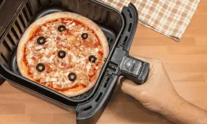 Une pizza garnie d'olives noires et de fromage est prête à être cuite dans un airfryer.