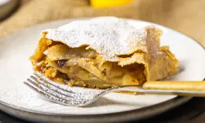 Ein Stück Apfelstrudel, bestäubt mit Puderzucker, wartet auf dem Teller. Dieses Apfelstrudel Rezept ist ein Genuss!