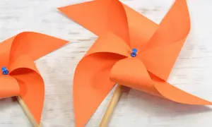 Zwei selbstgebastelte Windräder aus orangefarbenem Papier auf Holzuntergrund. Perfekt zum Windrad basteln mit Kindern.