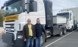 Deux chauffeurs poids lourd national posent devant leurs camions. L'un porte un gilet jaune, l'autre une veste bleue.