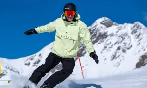 Snowboarder w jasnej kurtce i czarnych spodniach, z kaskiem i goglami, śmiga po stoku. Czy buty narciarskie pasują do snowboardu? Nie, to różne sprzęty.
