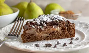 Una fetta di torta pere e cioccolato, cosparsa di zucchero a velo e gocce di cioccolato, con pere caramellate all'interno.