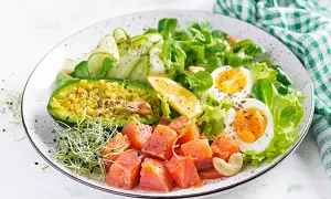 Un'idea per cosa mangiare a pranzo: un piatto colorato con salmone a cubetti, avocado, uova sode, cetrioli e germogli.