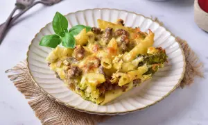 Pyszna zapiekanka makaronowa z mięsem mielonym w sosie śmietanowym, z brokułami i serem, udekorowana bazylią.